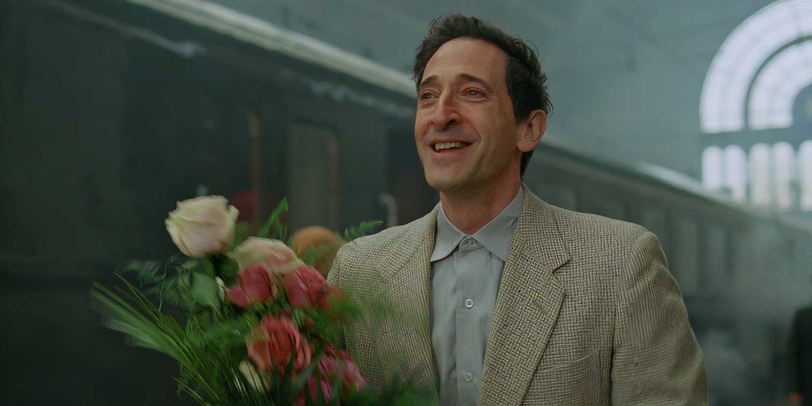 Adrien Brody in The Brutalist holding flowers at the train station