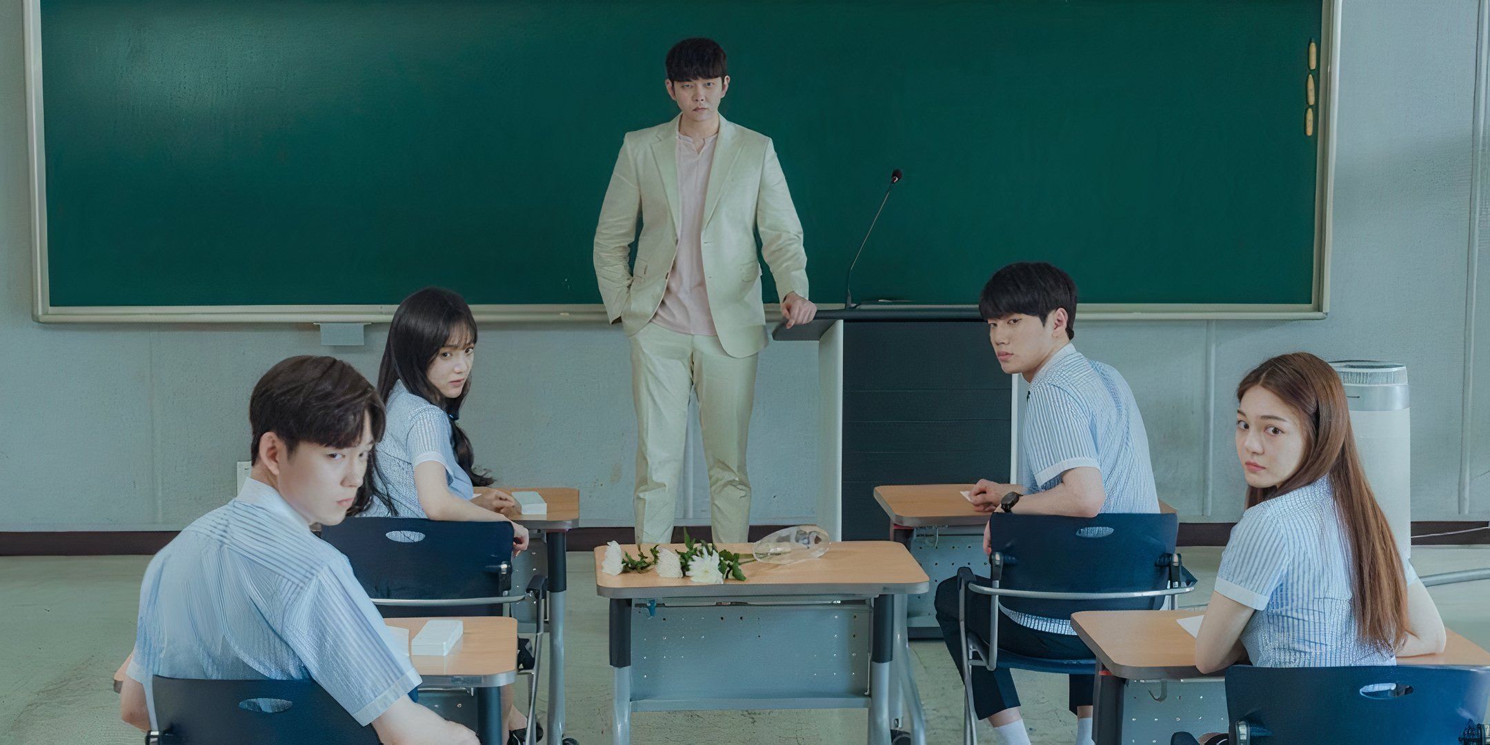 In a classroom, a professor stands in front of a chalk board and looks forward as his students are turned in their chairs looking in the same direction.