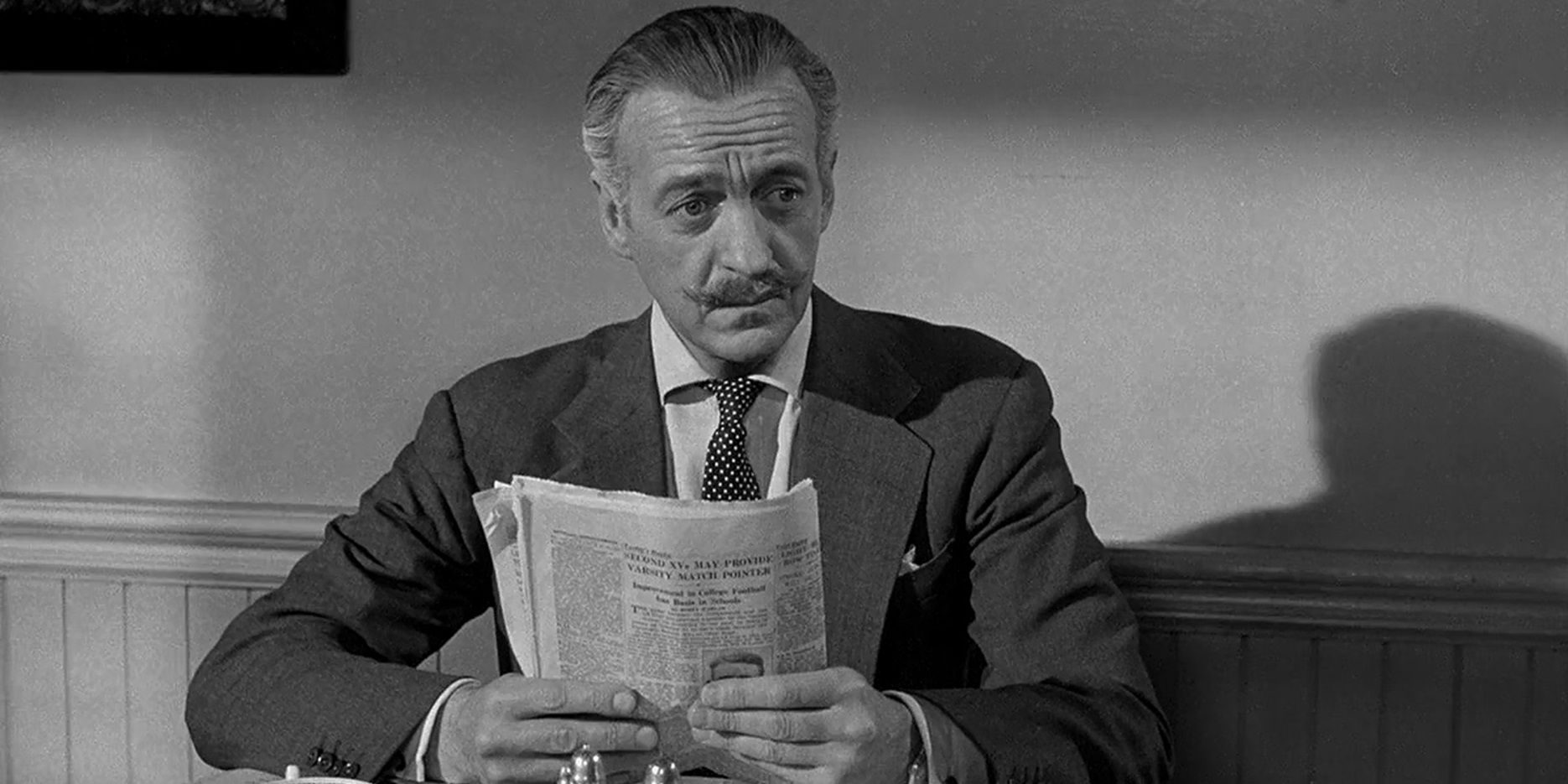 David Niven está leyendo un periódico en mesas separadas.