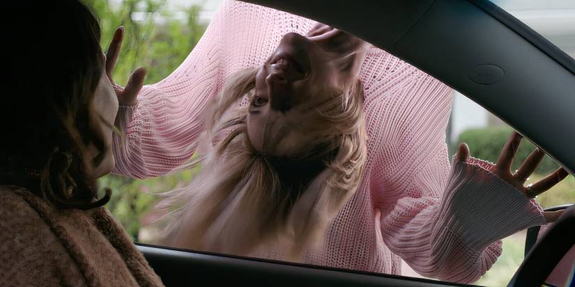 A young girl hangs upside down of the driver's side window of and smiles at Smile 2022 main protagonist Rose