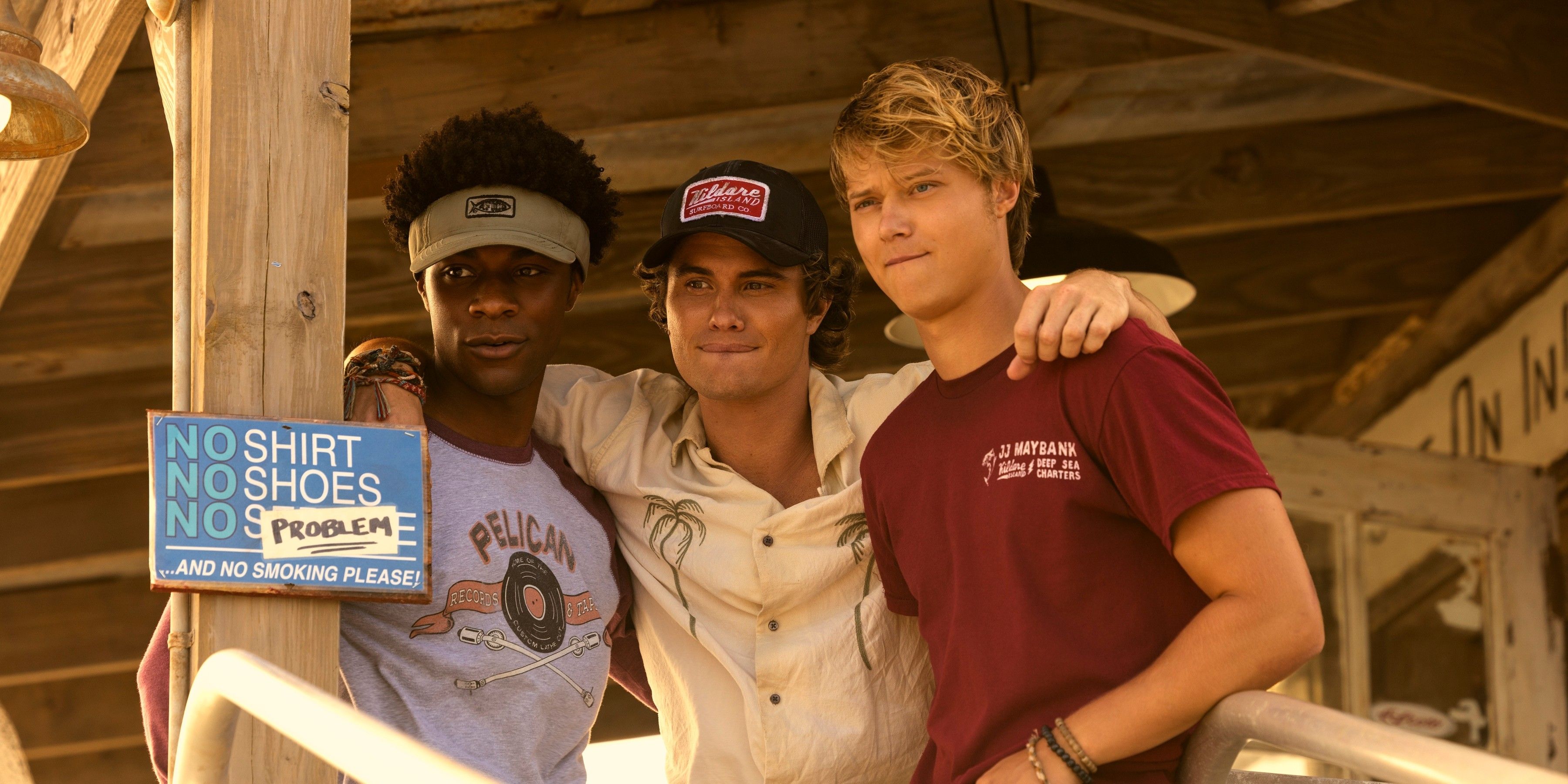 John B con sus brazos alrededor de Pop y JJ en la tienda de alquiler de barcos en la temporada 4 de Outer Banks