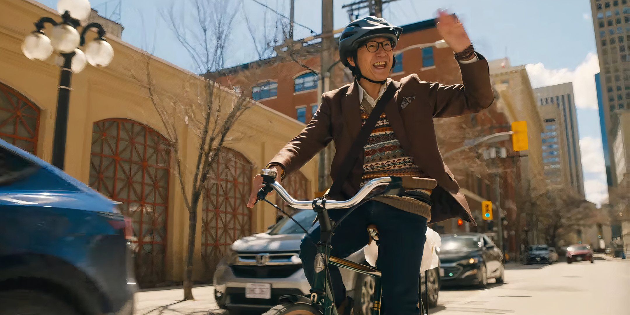 Ke Huy Quan as Marvin smiling and waving while riding his bike in Love Hurts