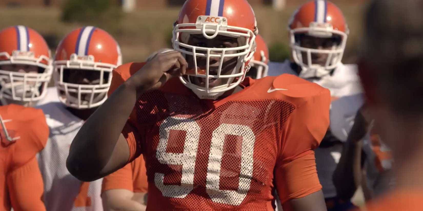 Luke Tennie wearing an orange #90 football uniform and biting down a mouthguard in Safety