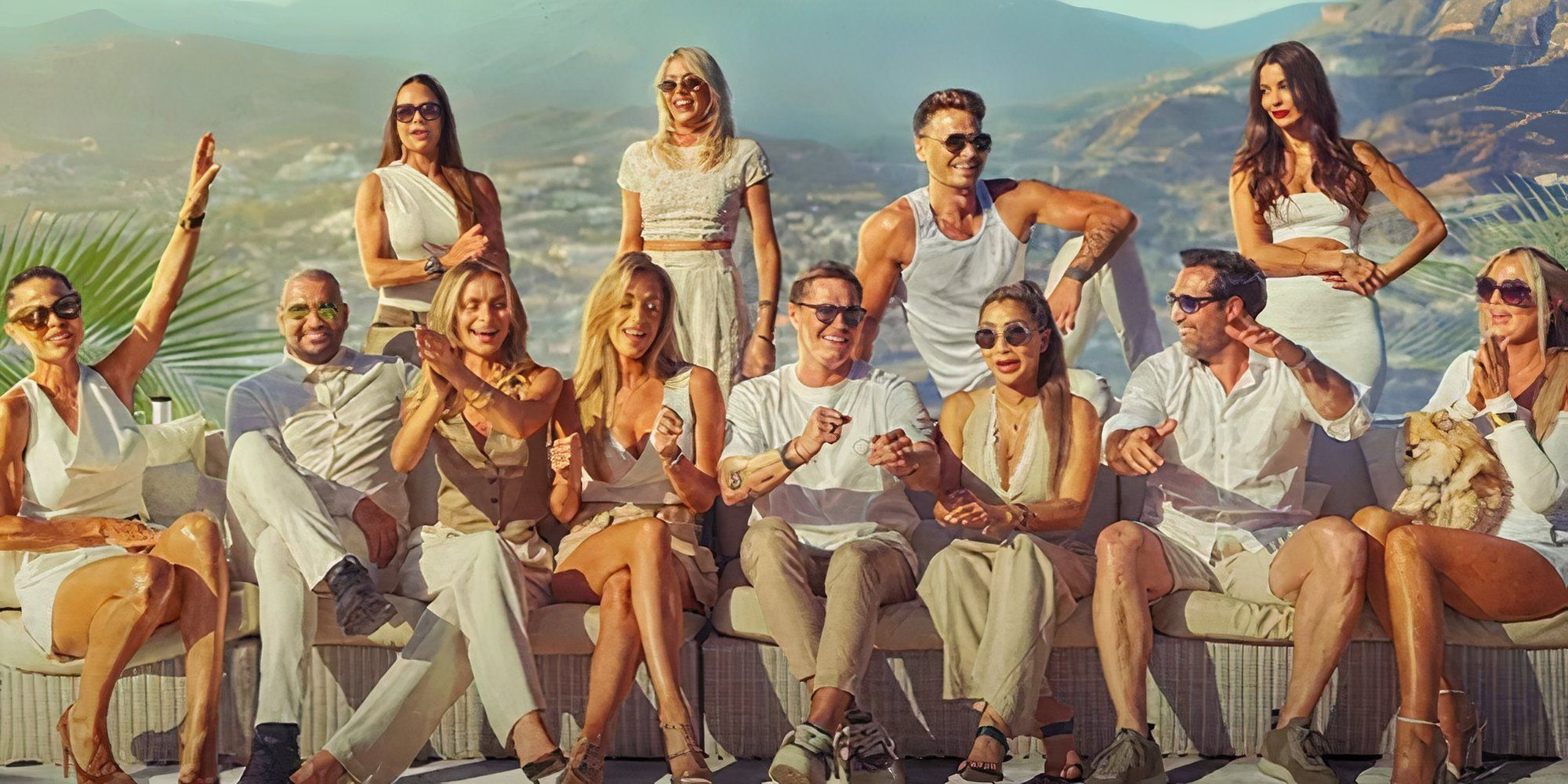 Os membros do elenco da 1ª temporada de Making It In Marbella com alguns sentados enquanto outros estão de pé e algumas colinas e propriedades visíveis ao fundo