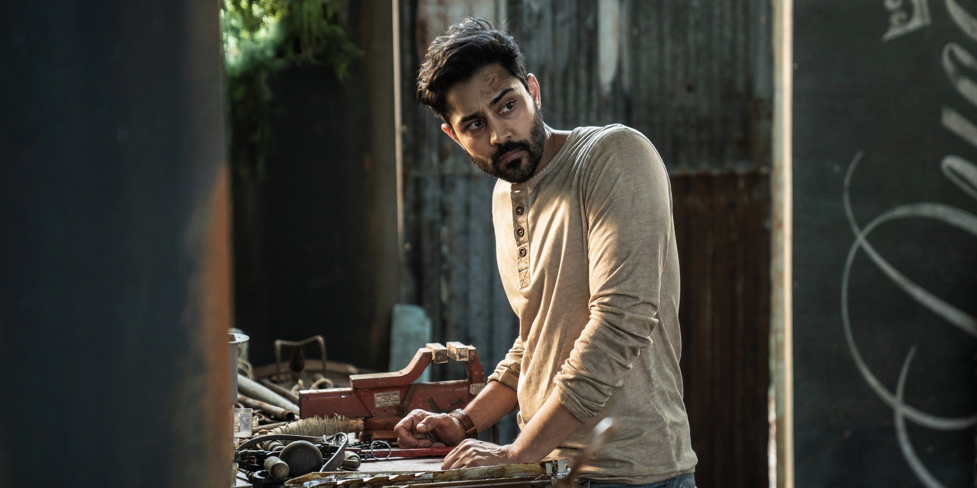 Manish Dayal as Ash leaning on his work bench in The Walking Dead Daryl Dixon season 2