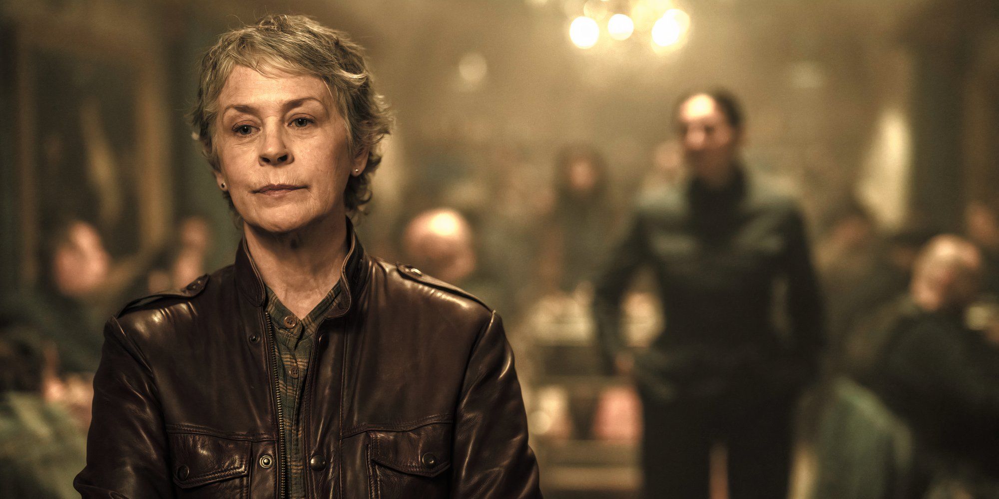 Melissa McBride como Carol parada en el comedor con Janet al fondo en Daryl Dixon Temporada 2 Episodio 3