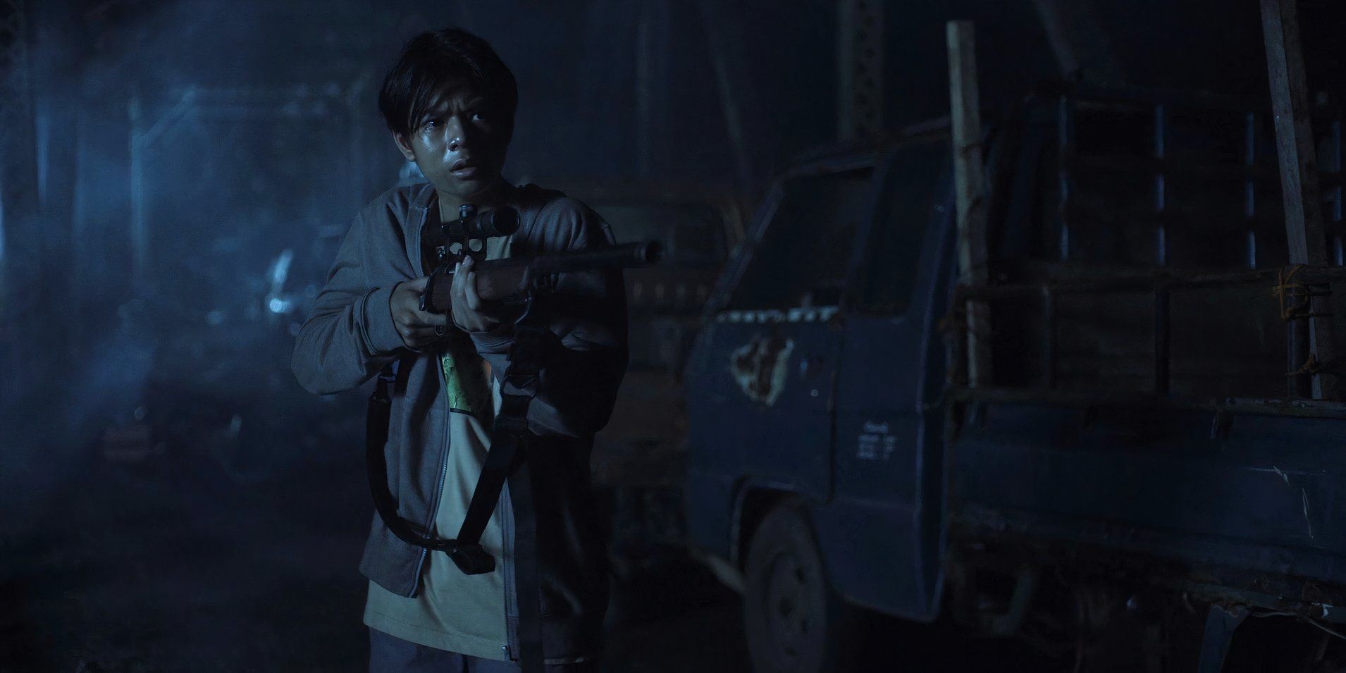 Joshua (Marco Masa) holding a rifle on the bridge in Outside