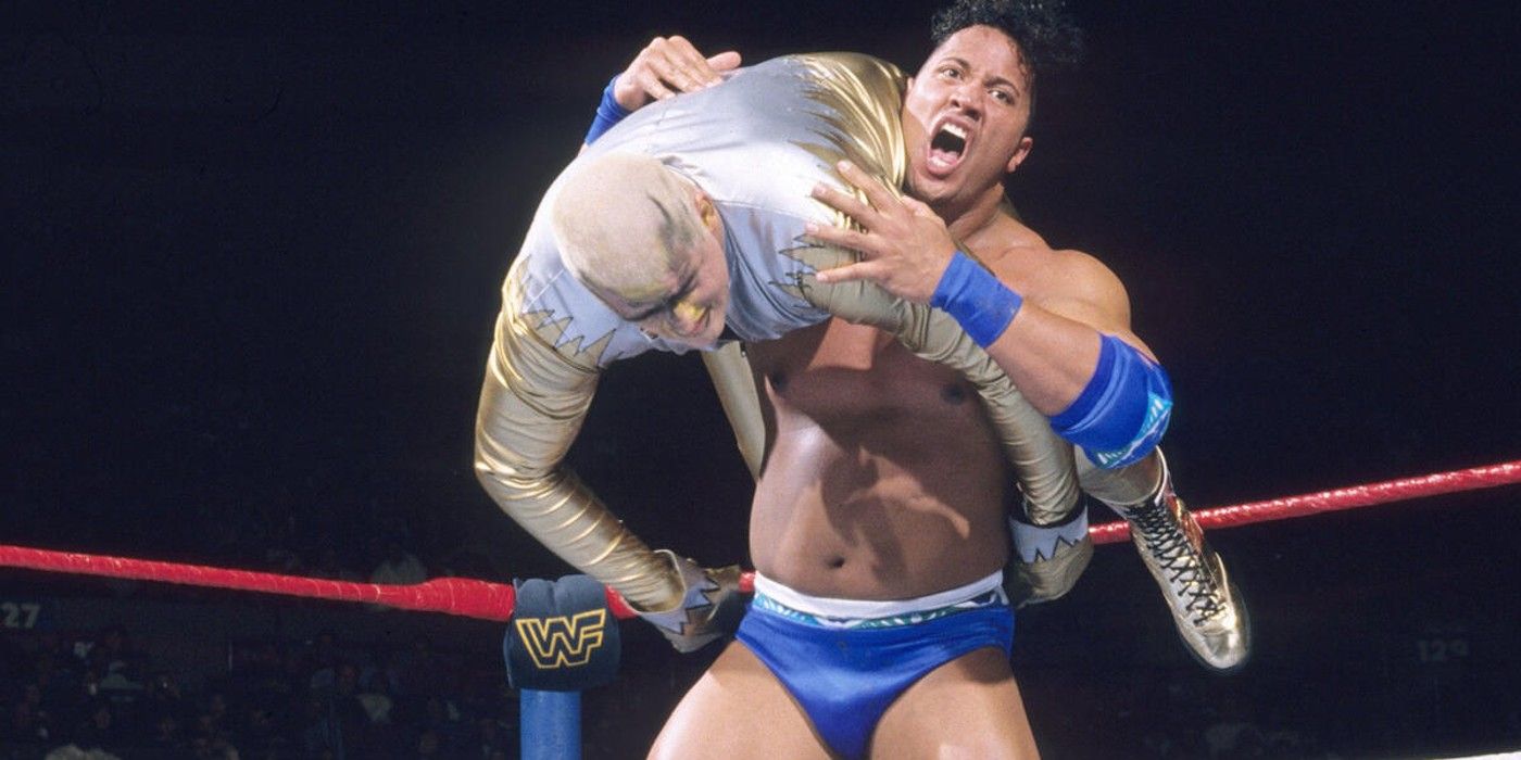 Rocky Maivia The Rock coloca Goldust em posição para um quebra-ombro dentro de um ringue da WWE