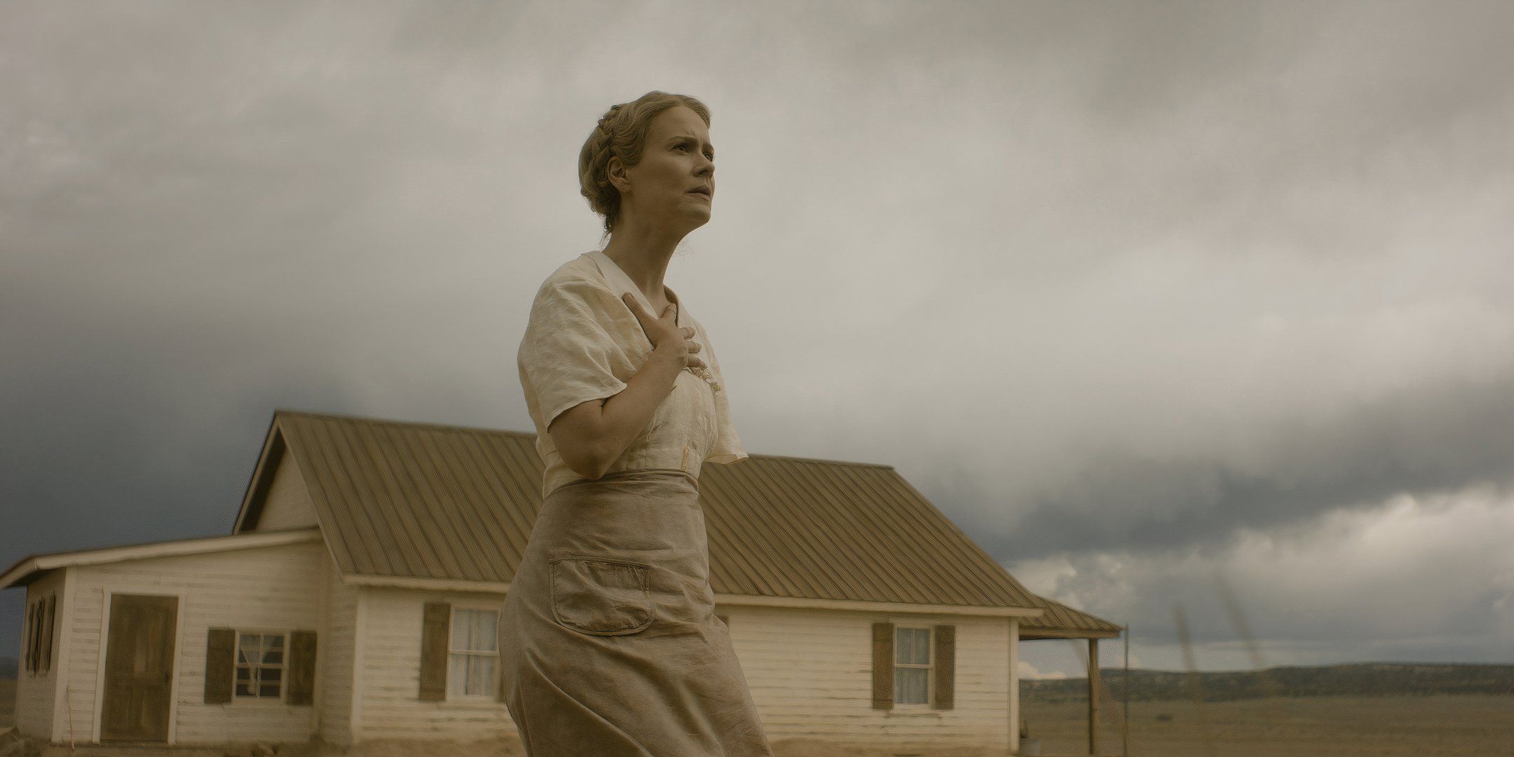 Sarah Paulson como Margaret mira sospechosamente con la mano en el pecho y la casa al fondo en una película. 