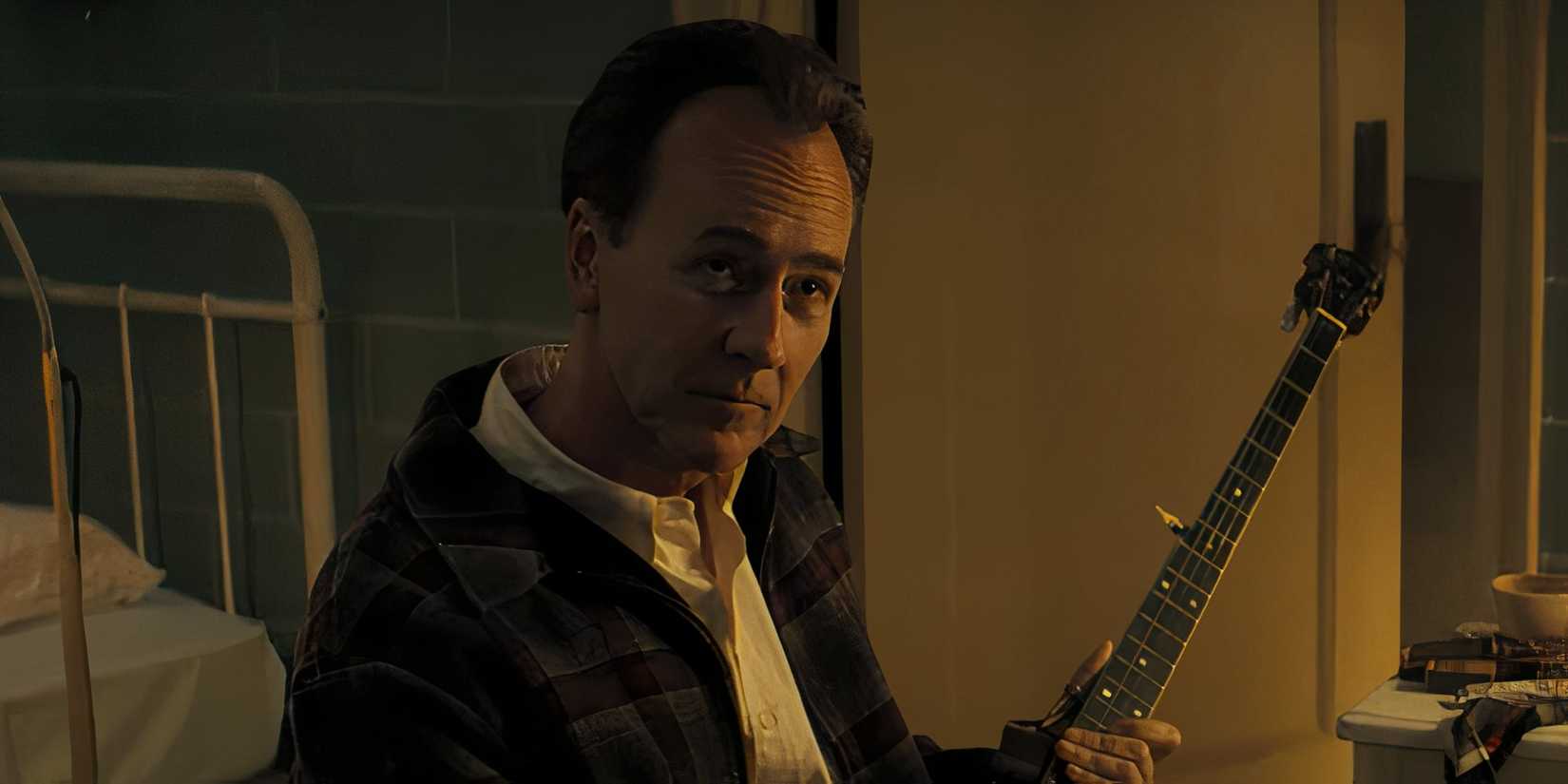 Pete Seeger (Edward Norton) holds an instrument as he smiles approvingly up at Bob Dylan.