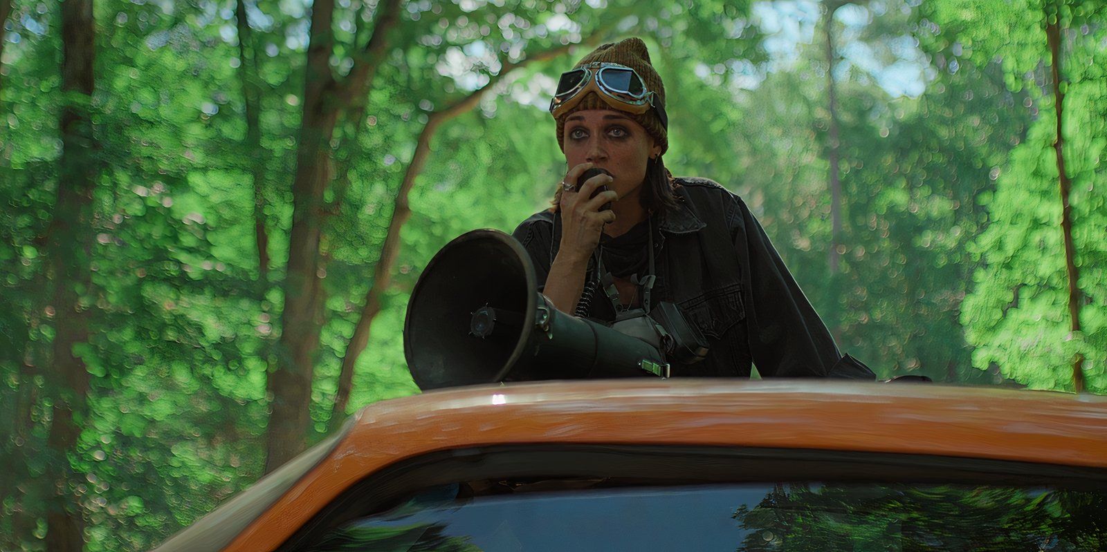 A woman leans on the top of a car and speaks through a megaphone in Teacup