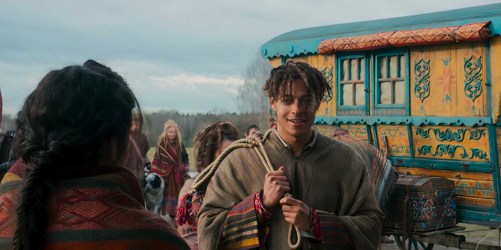 Aram stands in front of a colorful Tuatha'an wagon in The Wheel of Time