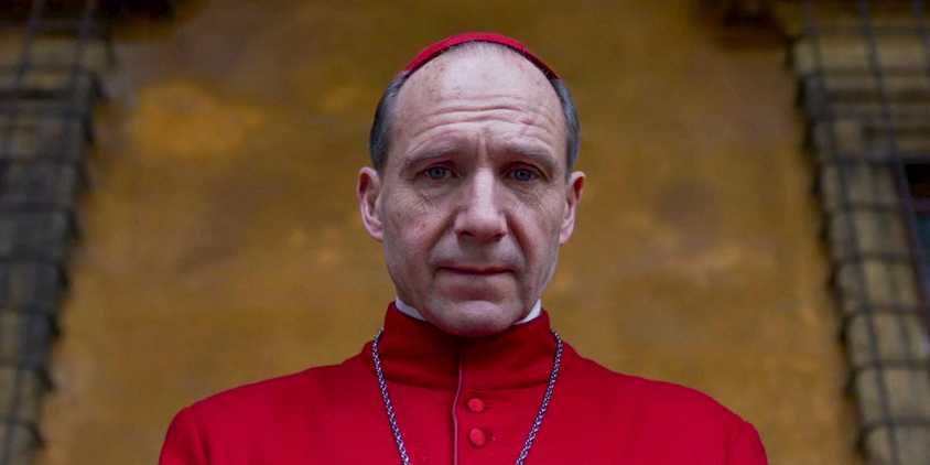 Ralph Fiennes in his red robes looking downward in Conclave
