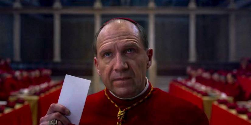 Cardinal Lawrence holding up a slip of paper while looking upwards in Conclave