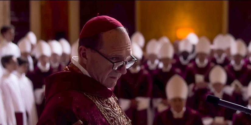Ralph Fiennes standing in front of the Cardinals looking apprehensive in Conclave