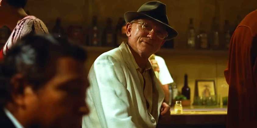 Daniel Craig sitting at a bar and looking out at someone in Queer
