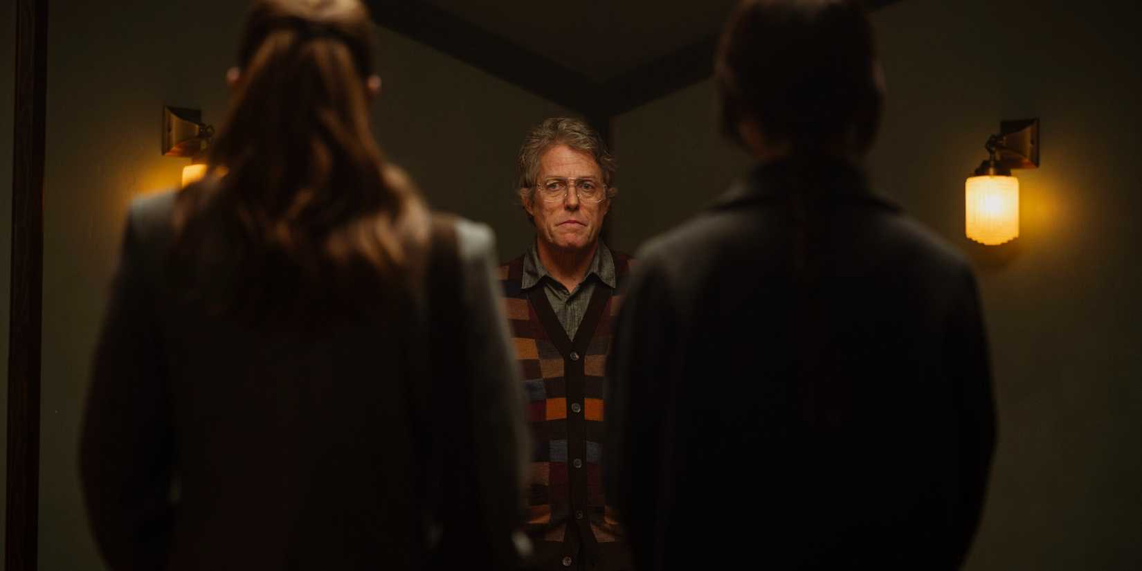 Hugh Grant framed between two girls, who stand with their backs to the camera, in Heretic