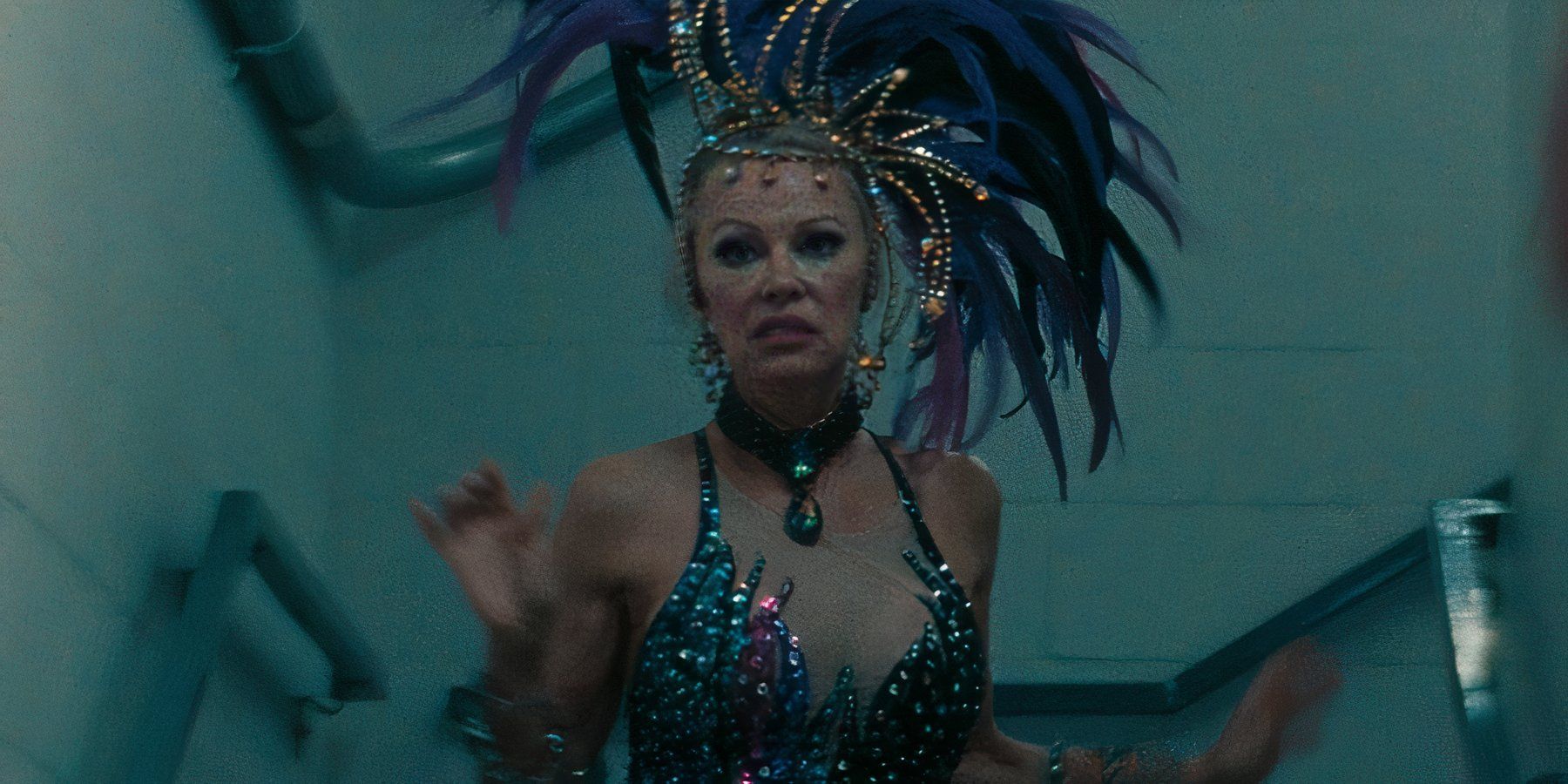 Pamela Anderson running down stairs in a feathered hat and blue sequined dress, looking stressed inin The Last Showgirl