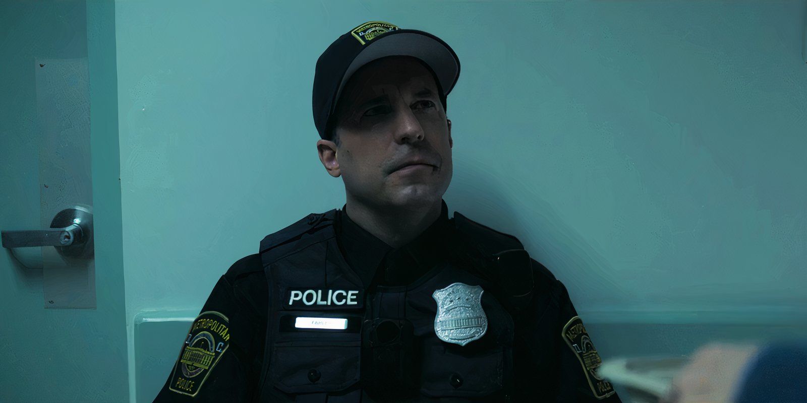 Officer Farley is sitting in a chair by a door in Cross season 1 episode 7