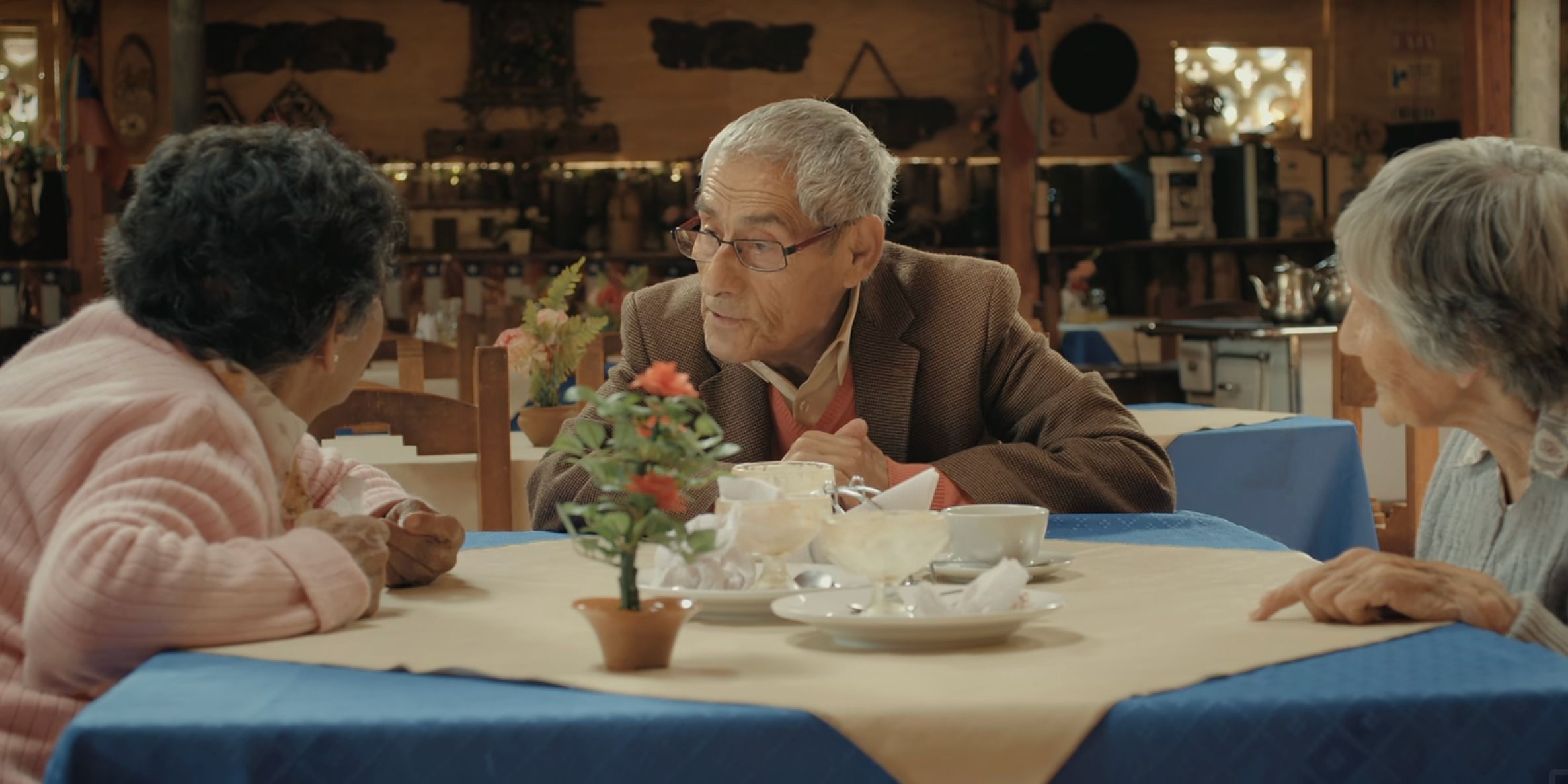 Sergio em O Agente Toupeira sentado em uma mesa com amigos