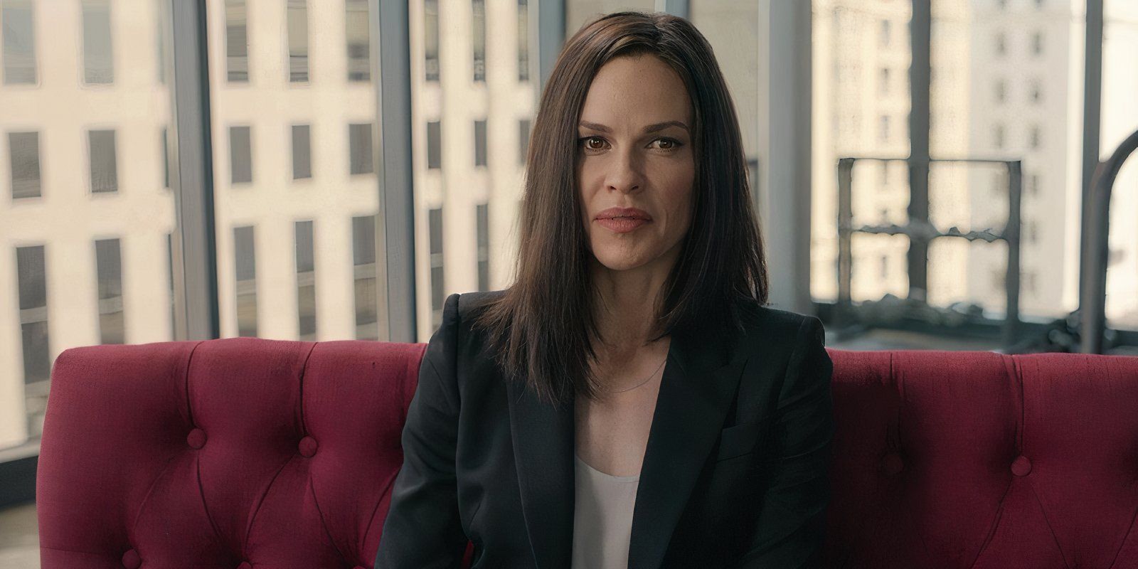 Hilary Swank sitting on a red sofa in The Hunt