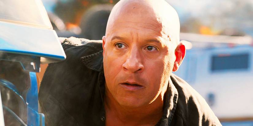 Vin Diesel taking cover behind a car as Dom Toretto in Fast X