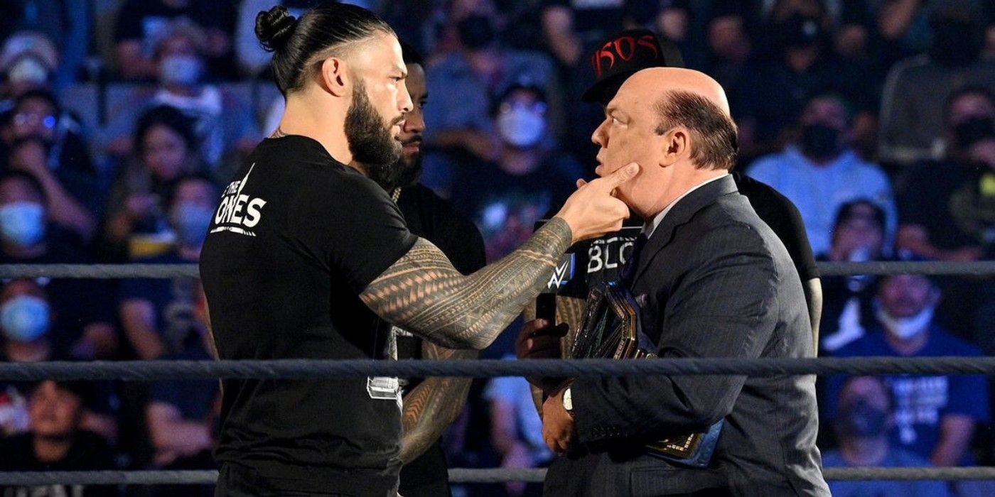 O campeão universal da WWE, Roman Reigns, agarra Paul Heyman pelo rosto na frente dos Usos no WWE Friday Night SmackDown