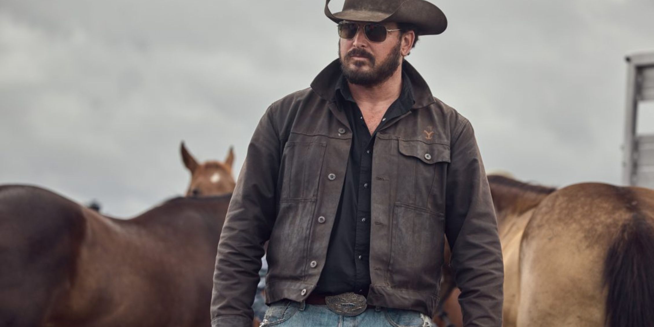 Yellowstone Rip con gafas de sol y un sombrero de vaquero observa a los vaqueros mientras están de pie con caballos