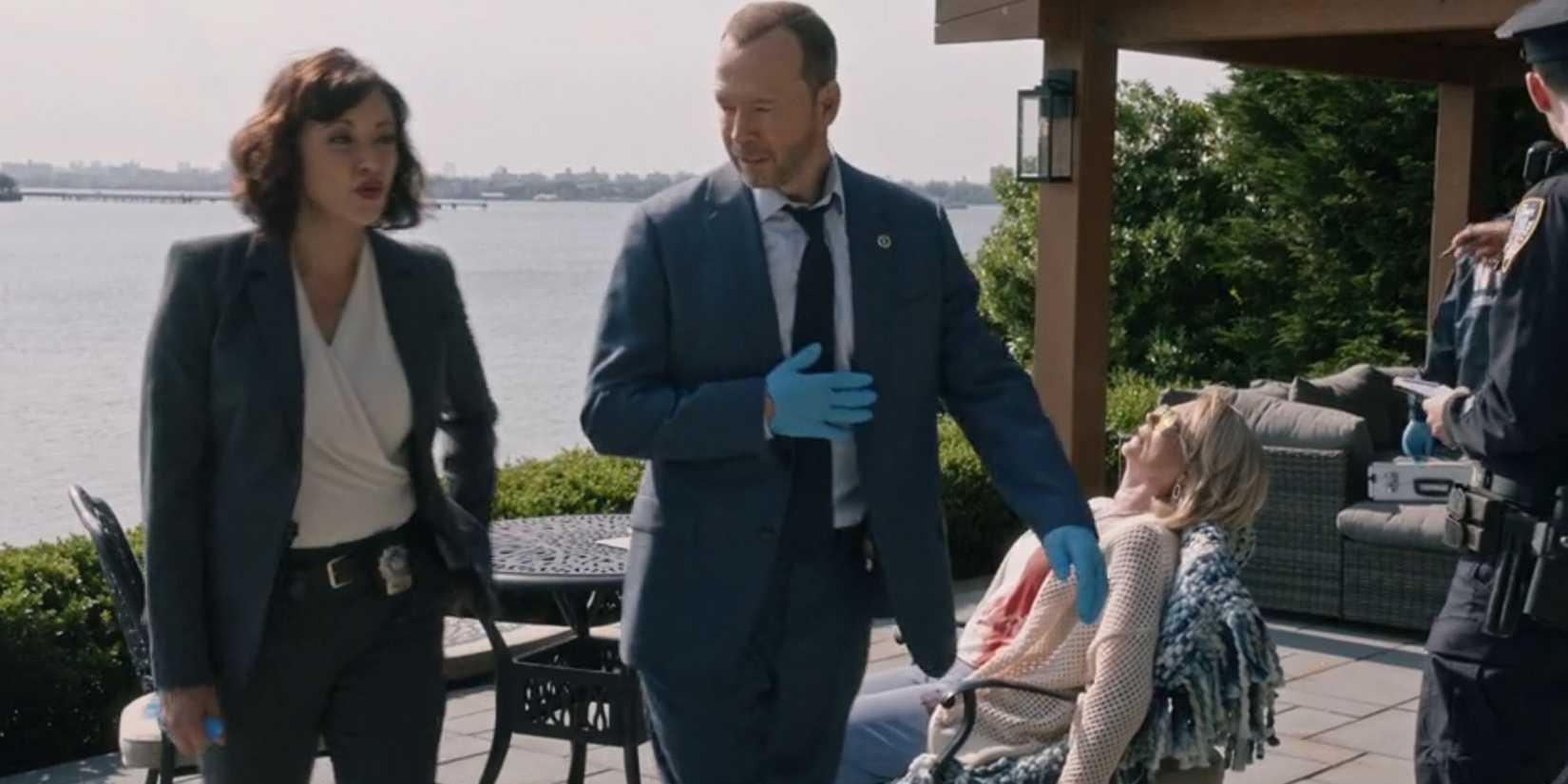Blue Bloods Danny And Baez wearing blue gloves while a dead body sits behind them in a deck chair