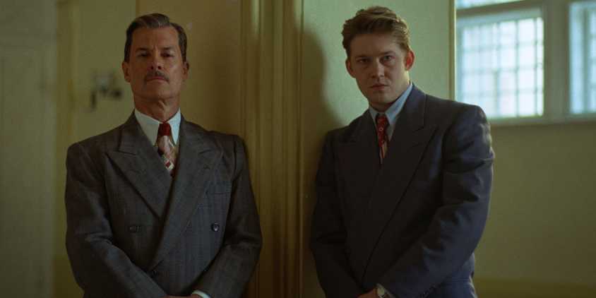 Harrison and Harry standing together in similar suits and poses in The Brutalist