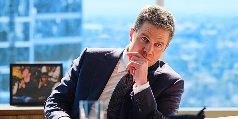 Stephen Amell as Ted Black sitting in an office chair near windows in Suits LA 
