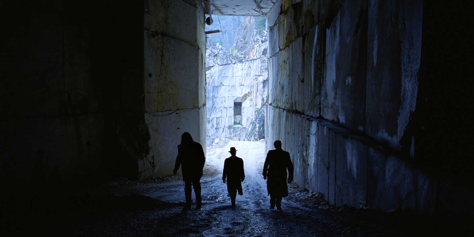 Three men in silhouette walking into the darkness of a marble quarry in The Brutalist