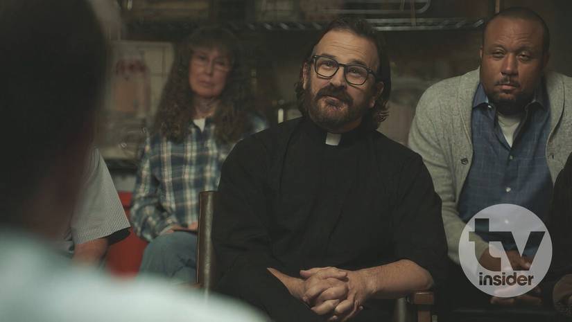 Reverend Phil (Speight Jr.) sitting in a chair surround by his faith-based sobriety group. His dressed in traditional priest-wear