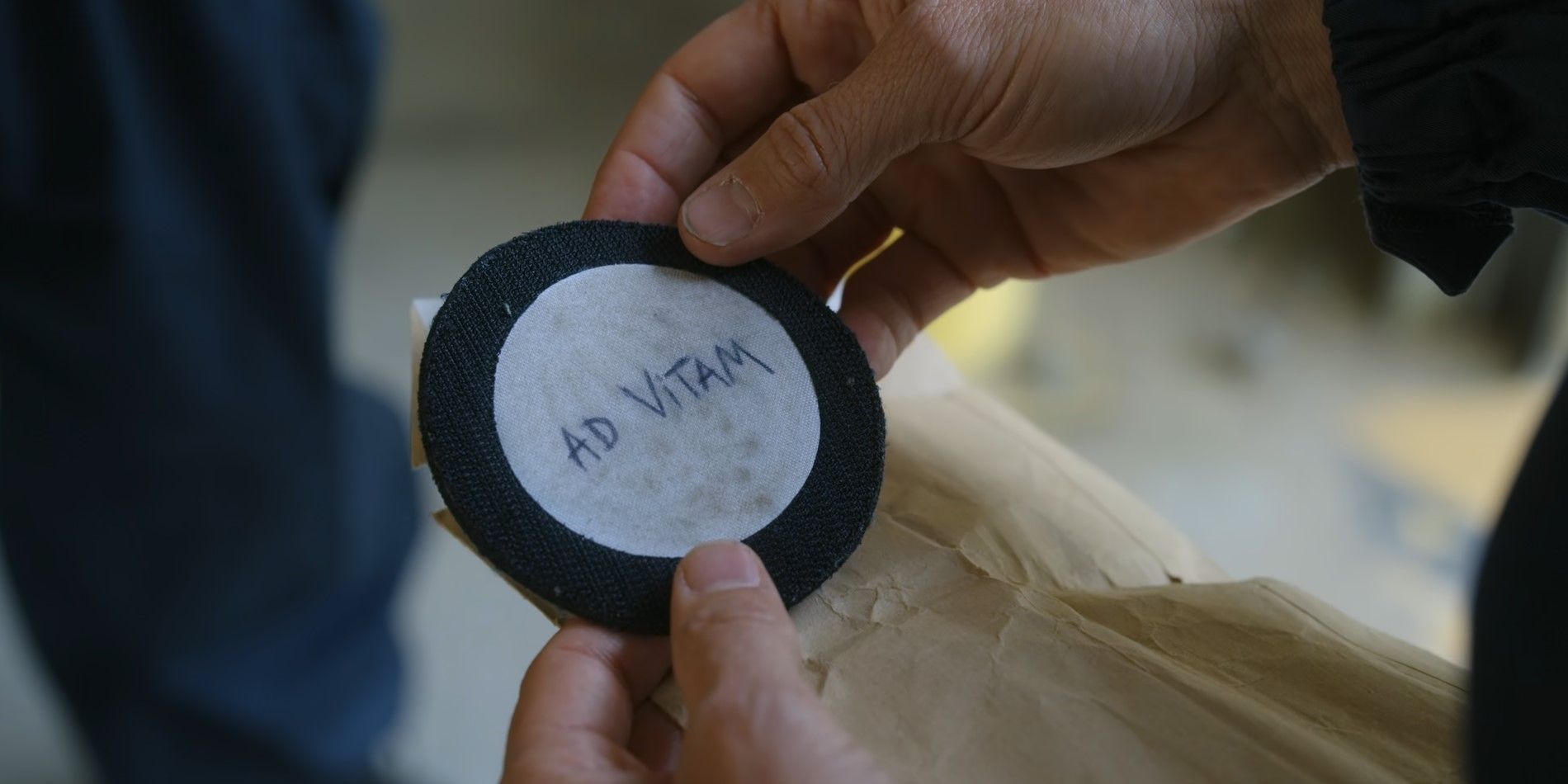 Franck holding a patch that reads "Ad Vitam" in Ad Vitam