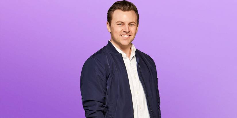 Love is blind season 8 Daniel Hastings in a never blue jacket and white shirt with his hands in the pocket.
