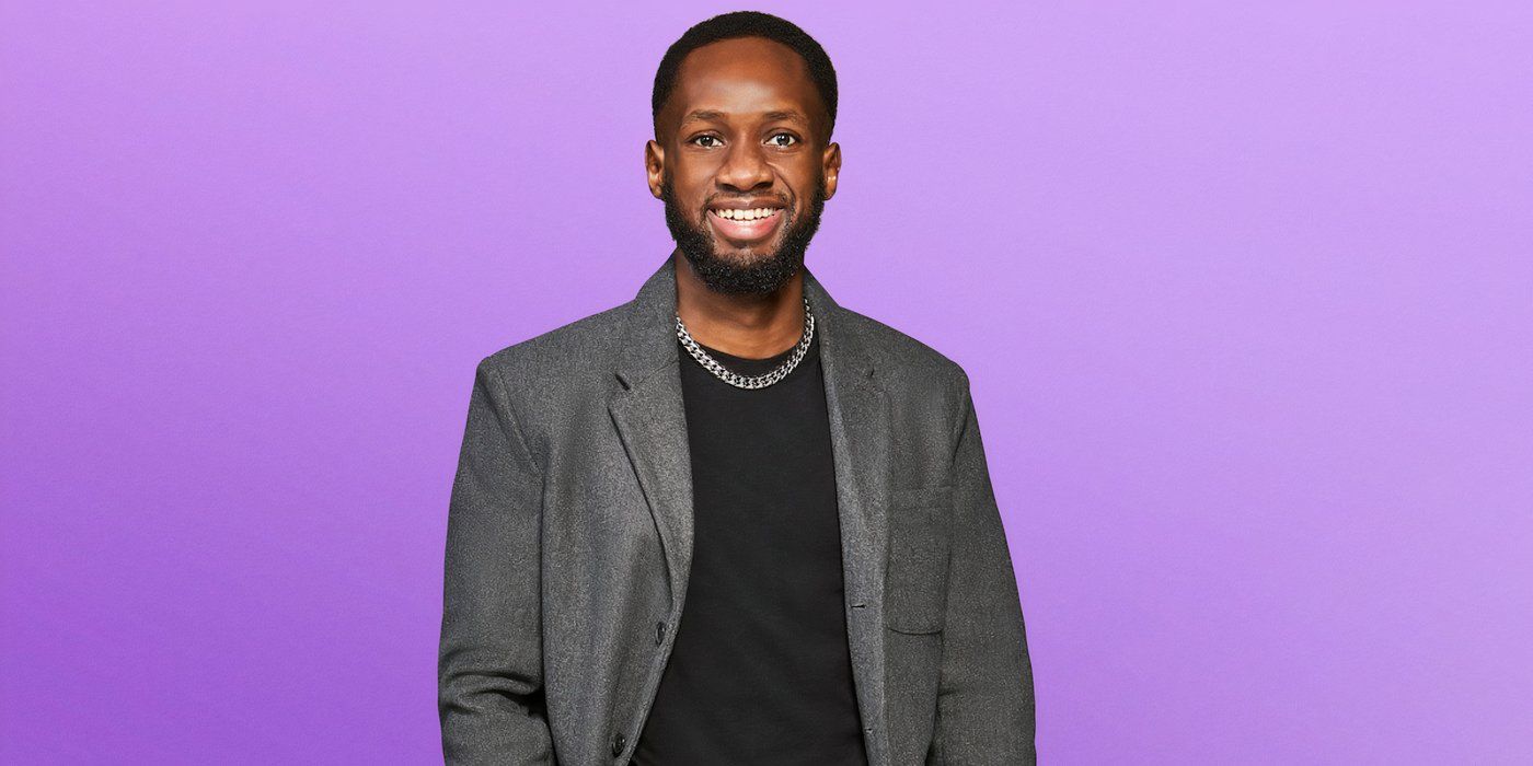 Love is Blind Season 8 Hugo Orieny wearing a black t -shirt, gray jacket and a silver chain smiling during promotional filming