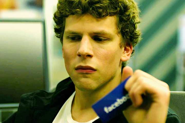 Jesse Eisenberg as Mark Zuckerberg looking sad while holding onto a Facebook card in The Social Network