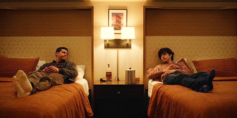 Dylan O'Brien and James Sweeney laying on separate beds in a hotel room
