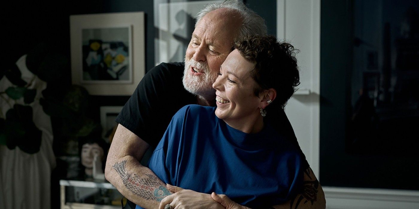 John Lithgow hugging Olivia Colman from behind as both smile in Jimpa