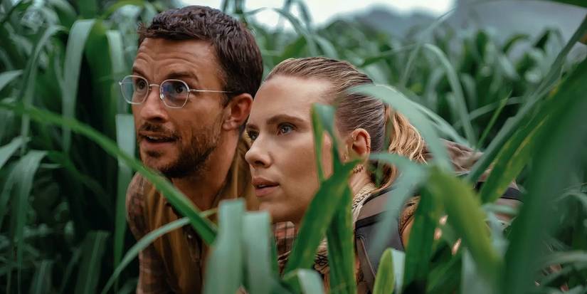Jonathan Bailey and Scarlett Johansson crouching among high grass in Jurassic World Rebirth