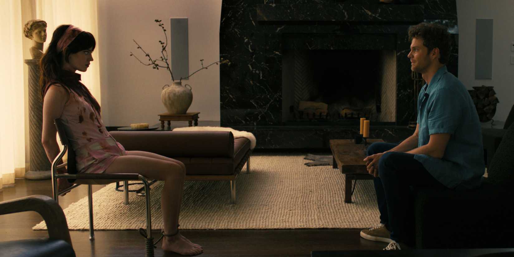 Josh seated across a bloodied Iris, who is tied to her chair, in Companion