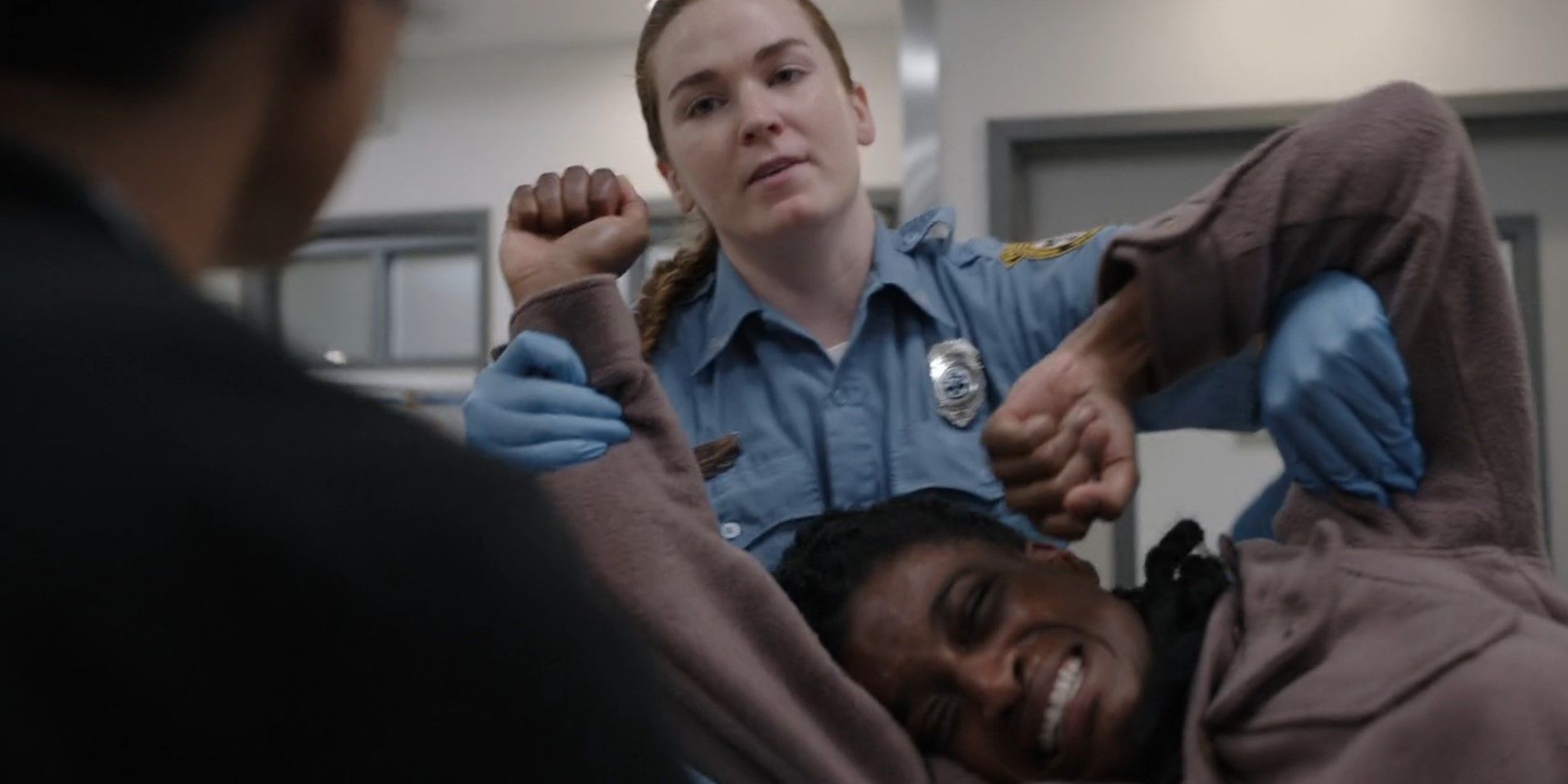 Joyce St. Claire (Ashley Romans) writhing in pain while a paramedic restrains her in The Pitt season 1, episode 2