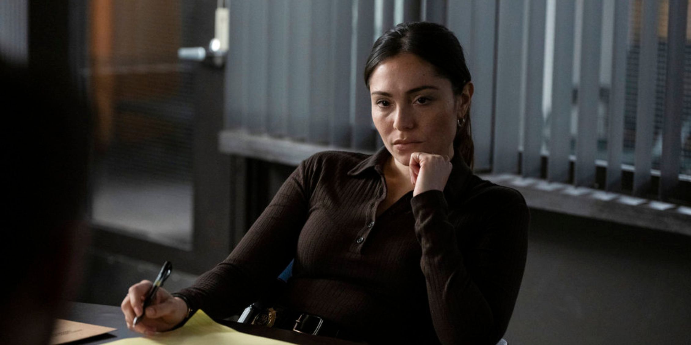 Law & Order SVU Silva sentada em sua mesa parecendo pensativa e escrevendo em um bloco de notas amarelo