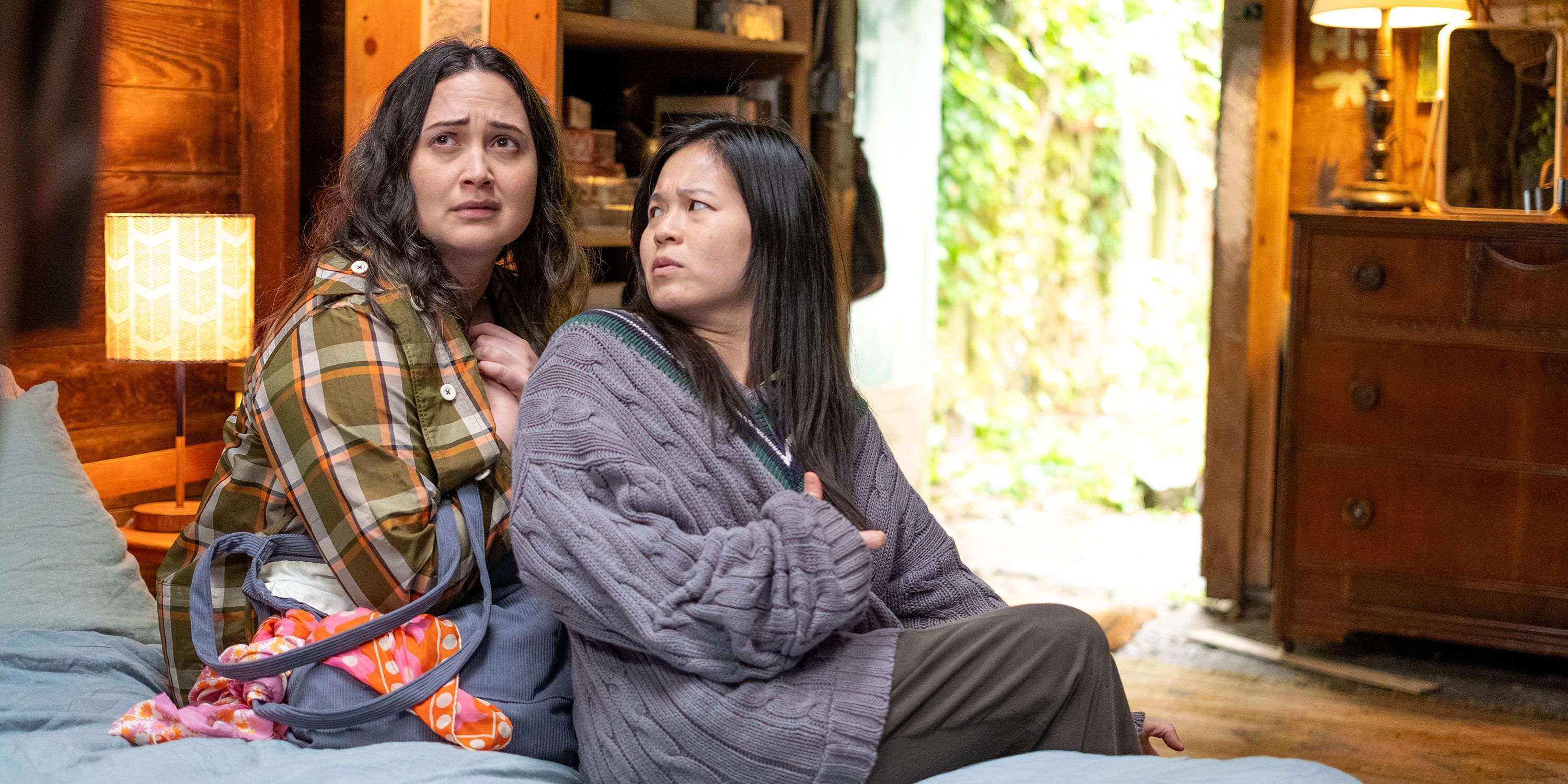 Lily Gladstone and Kelly Marie Tran sitting on a bed in The Wedding Banquet