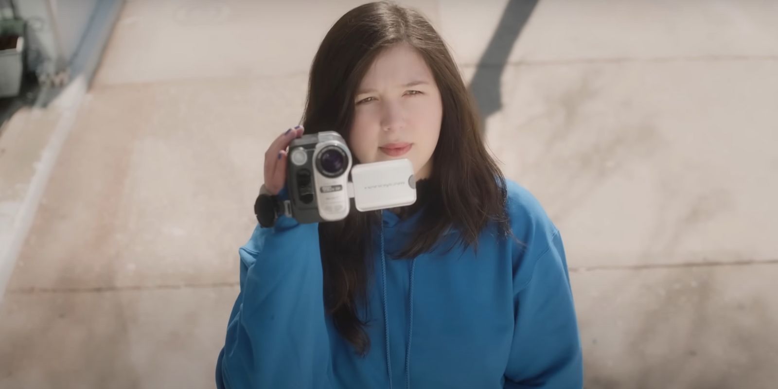 Lucy Dacus in a blue hoodie holding a camcorder for the &ldquo;Hot and Heavy&rdquo; music video