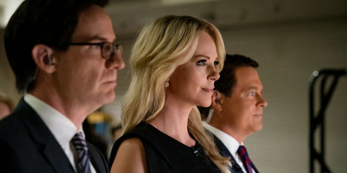 Megyn Kelly (Charlize Theron) is between two executives and smiling in a bomb.