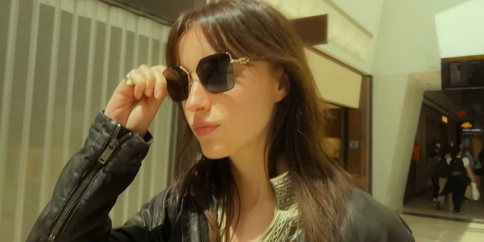 Phoebe Dynevor's Maya walking casually while putting on sunglasses in Inheritance