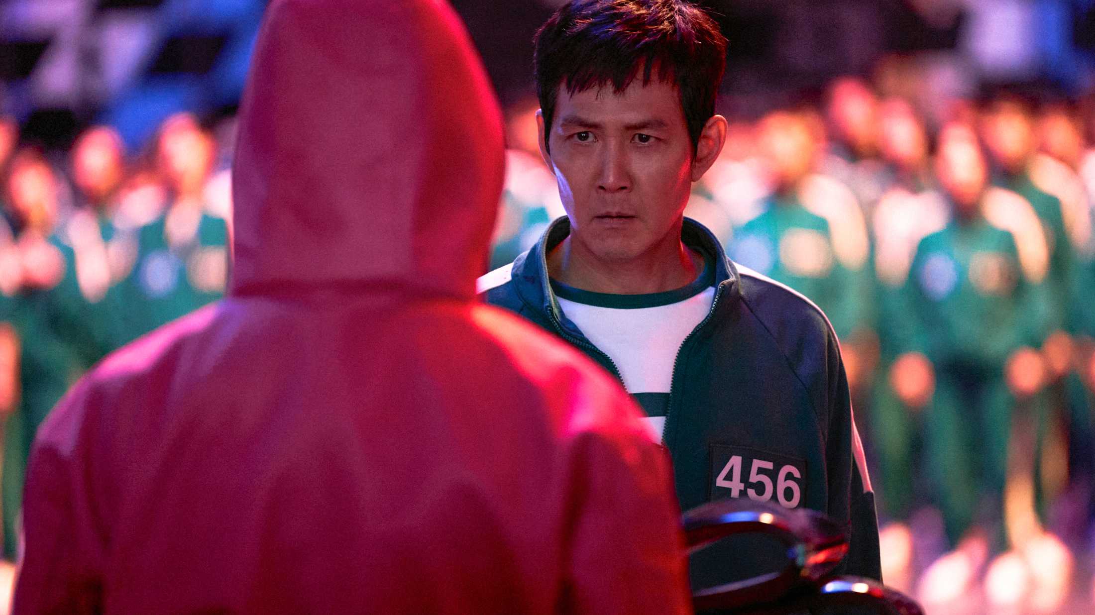 Seong Gi-hun (Lee Jung-jae) in front of one of the guards, about to vote for the game to end in Squid Game Season 2