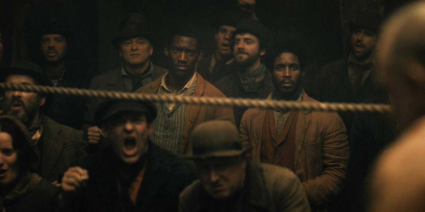 Hezekiah (Malachi Kirby) and Alec (Francis Lovehall) as spectators at a wrestling show in A Thousand Blows Season 1 Ep 1