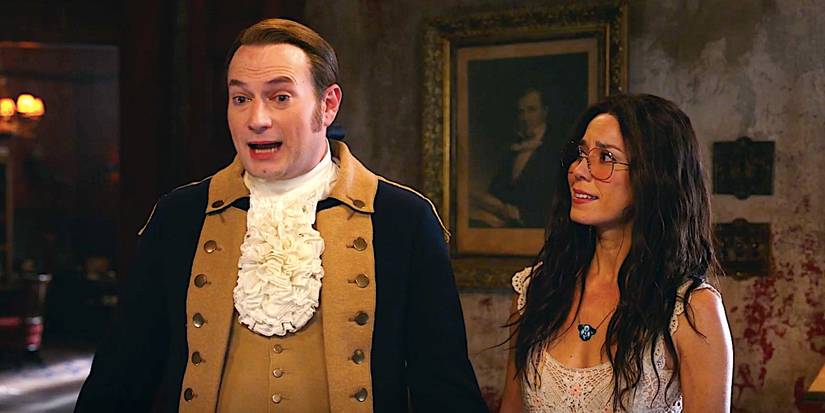 Brandon Scott James' Isaac and Sheila Carrasco's Flower stand talking in a living room in Ghosts season 4 episode 11